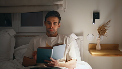 Man reading book bedroom feeling serene and relaxed mood at night closeup.