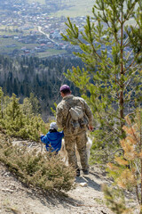 A man in a military uniform comes down from the mountains with a little boy and a dog. Mountainous terrain. Mountain landscape. Rear view