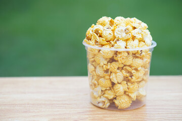 Popcorn in glass bowl on wooden table against green background, made from seeds of maize or corn by baking or heating, mixed with salt, sugar and butter caramel. Concept, delicious snack. 