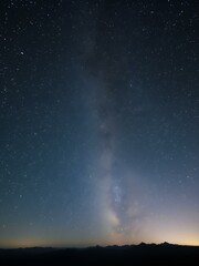 Obraz premium A stunning night sky filled with countless stars, the Milky Way glowing brightly across the horizon, and soft silhouettes of mountains in the distance 