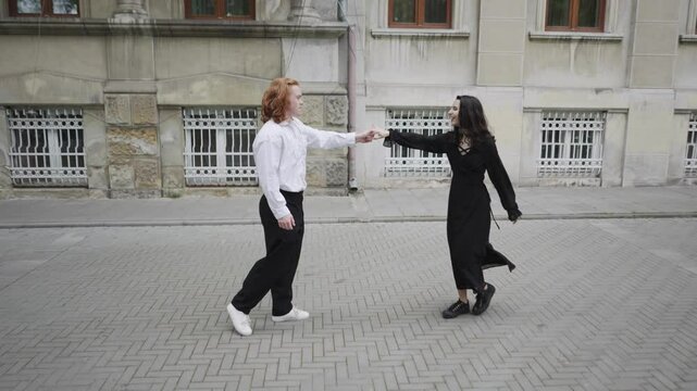 A lively scene unfolds as a couple dances joyfully on a sidewalk