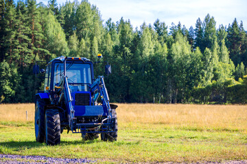 Fototapeta premium Blue tractor mowing grass in field on summer sunny day