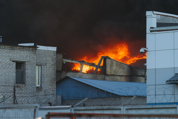 Massive large blaze fire in the city, blazing warehouse factory, storage building is burning, firefighters team putting out the fire, firemen on duty, extinguish the fire, arson, burning house damage