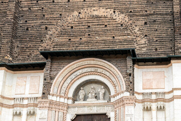 Facade detail of Basilica of San Petronio with red bricks, white marble, and sculptures, Bologna, Italy