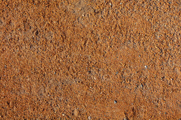 A close up of a sandy surface with a lot of small rocks. The image has a somewhat rough and rugged appearance, with the rocks scattered throughout the surface. Scene is somewhat desolate and barren