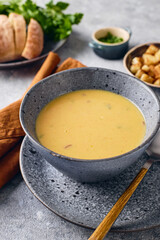 Bowl of potato soup puree with croutons, parsley and ground red pepper, and spoon on the plate.