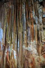 Colorful stalactites hang from the cave ceiling, showcasing mineral formations with a blend of earth tones. The exploration reveals nature's artistry in every dripstone.