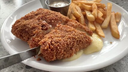 4k footage, close up hand and knife cutting fried chicken cordon bleu set of plate with French fries and side dishes, seen the mozzarella cheese melt and flows out of the chicken meat.