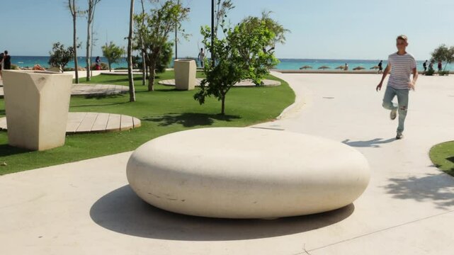 Energetic parkour enthusiast vaulting over large stone centerpiece in scenic seaside park, showcasing skill and agility