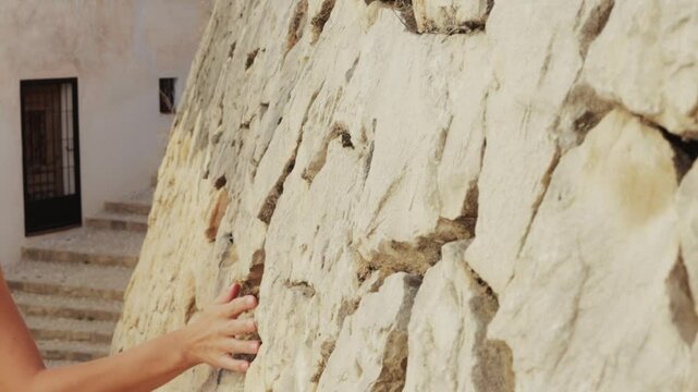 Tourist woman walk upstairs in mediterranean village, touch stone wall and enjoy summer holiday in charming, picturesque setting filled with history and culture