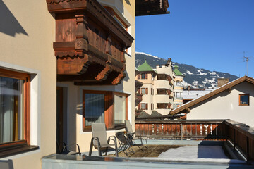 A large balcony made of carved wood of a winter ski hotel on which there are chairs for relaxation