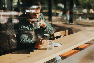Toughtful man savoring coffee alone at a cozy cafe on a sunny day while lost in contemplation by the window