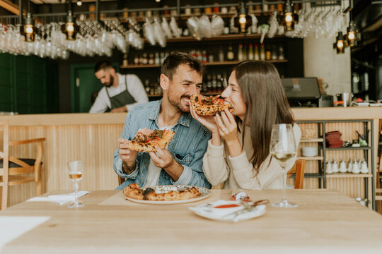 Enjoying delicious pizza together at a cozy restaurant with friends during a lively evening gathering - Powered by Adobe