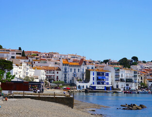 Obraz premium view along the promenade of Cadaqués, to the beautiful white houses, Port Alguer and the turquoise water of the Mediterranean Sea, mountains of the Pyrenees behind, Girona, Catalonia, Spain