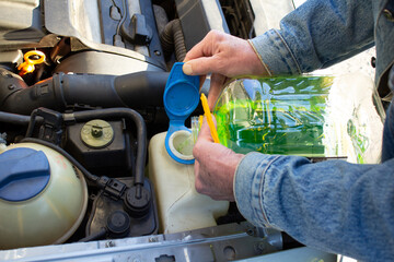 Car maintenance. The technician pours washer fluid into the car's reservoir.