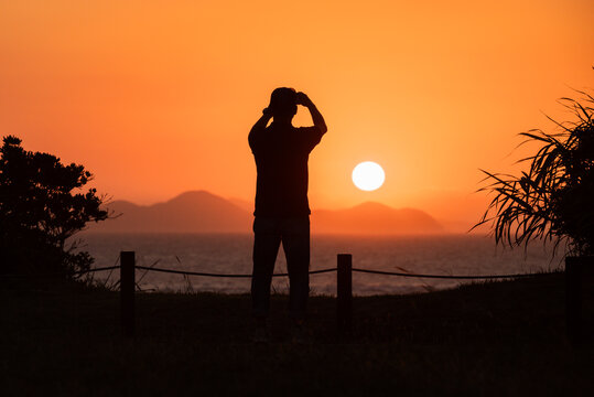 A silhouette of a man taking a photo of the sunset with his phone in Ashiya Town, Fukuoka, Japan