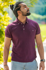Close-up portrait of a confident, handsome, bearded Asian-Indian man with a ponytail. He's gazing...