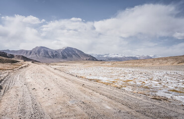 Dusty road of the Pamir Highway winds and twists in the valley of the Tien Shan mountains in Tajikistan in Pamir, landscape in the high desert mountains for background