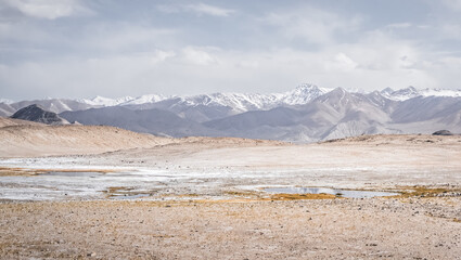 Panoramic landscape of textured Tien Shan mountains in Pamir in Tajikistan, landscape of a mountain range with snow and glaciers in summer, a small lake and reflection of mountains in it