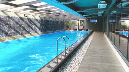 small indoor swimming pool empty in hotel or fitness club, green palm tree and sun loungers