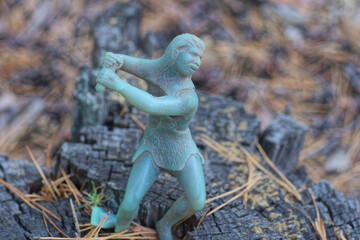 one old gray green plastic toy savage neanderthal stands on a wooden stump on a summer street