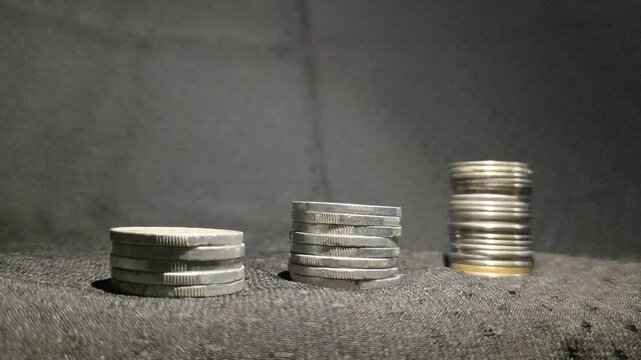 Three stack of coins aligned to form a revenue growth graph with a black background and moving light.