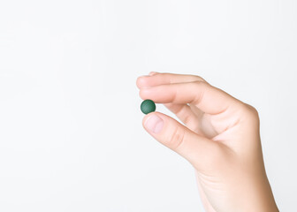 hand holding green chlorella and spirulina pill on grey background