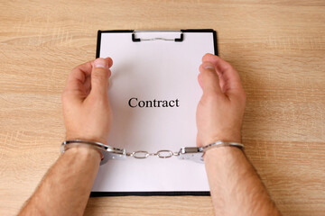 A man in handcuffs holds a document with the inscription 