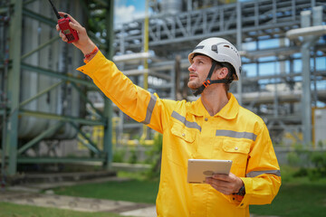 portrait oil refinery worker wears safety and harthat, holding tablet computer and walkie talkie inspection at oil refinery