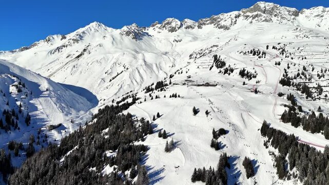 St Anton am Arlberg, Austria: Aerial view of famous bustling ski resort in Tyrolean Alps. Snow-covered slopes with ski runs, sunny day with clear blue sky - landscape panorama of Europe from above

