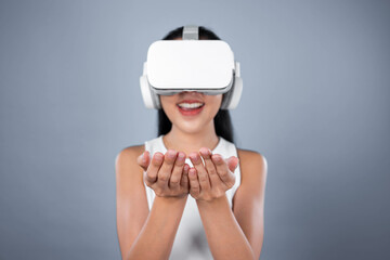 Smart female standing with gray background wearing VR headset connecting metaverse, futuristic cyberspace community technology. Elegant woman excited seeing generated virtual scenery. Hallucination.