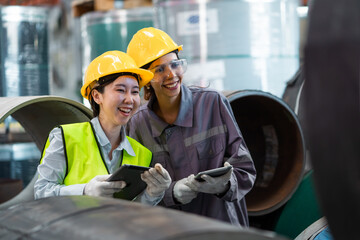 Two women wearing safety gear and holding tablets, smiling at the camera. Scene is positive and...