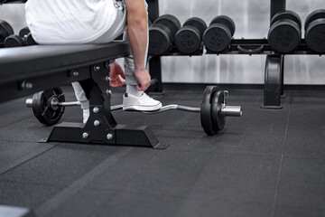 A man in a gym preparing to do an exercise with an EZ bar on a bench.