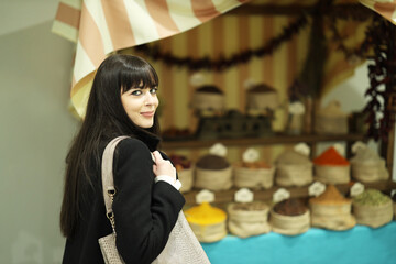 Lovely Caucasian modern girl in front of stall market stand counter, with spices, seasonings and ingredients. Exotic shopping of food cuisine. Concept smart young woman lifestyle scenes