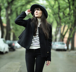 Lovely Caucasian modern girl with hat female beauty walks down the street alley on the tree-lined street. Concept young girls lifestyle scenes
