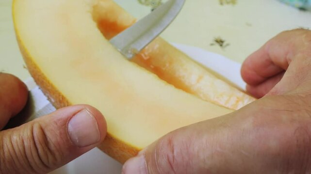 Long pieces are cut off from a melon cut lengthwise with a knife. Medium shot.