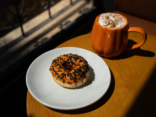 Autumn pumpkin spice latte in an orange pumpkin mug with a whipped cream and cinnamon, orange glazed donut 
