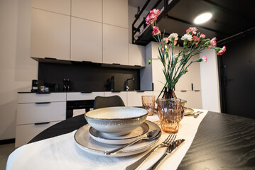 Luxury table setting in a modern kitchen with a vase of flowers. Modern furnished kitchen and a dining room. Modern kitchen connected to the living room in a small modern apartment.