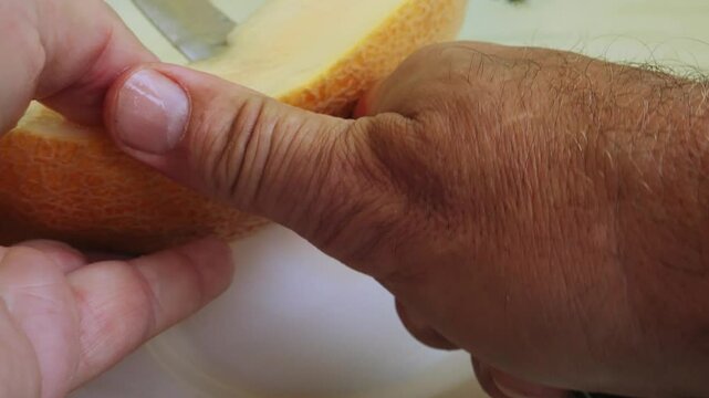 Long pieces are torn off with a knife from a juicy melon cut lengthwise. Medium shot.