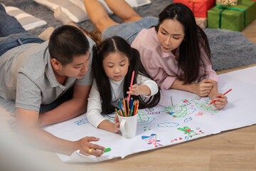Heartwarming scene of Asian family spending quality time together at home. The father, mother, and their young daughter are lying on the floor