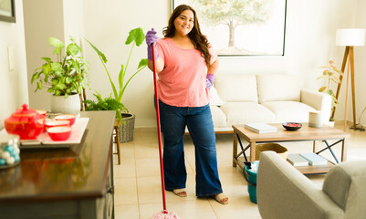 Plus size woman posing with her cleaning supplies while mopping the floor and doing household chores