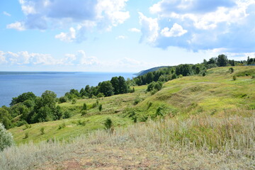 Naklejka premium a green hill with a view of the lake and trees and blue sky with clouds 