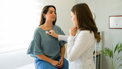 Doctor in lab coat using stethoscope to listen to female patient's heartbeat in a medical office