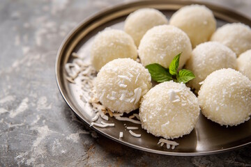 Coconut laddu coated in shredded coconut, served on a metal tray with mint leaves, offering a fresh and tropical twist on traditional Indian desserts for festivals like Diwali or Raksha Bandhan