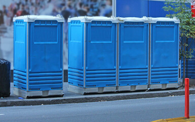 Four blue plastic Portable toilets op the foot path of a city street