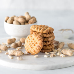 A stack of fresh homemade peanut butter cookies surrounded by peanuts.