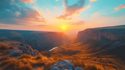 Fototapeta premium A stunning sunset over a vast canyon with a river winding through the valley, casting a warm glow over the landscape.