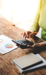 Close-up of young woman's hand working with tax and accounting documents using laptop and calculator to calculate financial transactions, taxes, company income. Finance and tax concepts