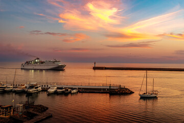 Fototapeta premium yacht enters marina as ferry enters commercial harbor next to lighthouse in beautiful sunset