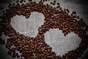 The image shows a close-up of dark, roasted coffee beans. One bean is in focus, highlighting its natural seam. The rest are blurred, creating a rich, textured background.

